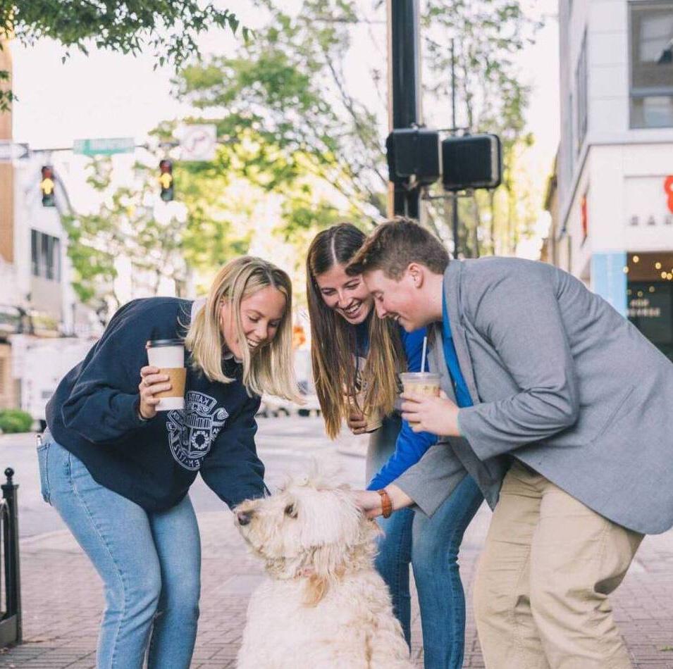 Three students petting a dog in downtown Winston Salem
